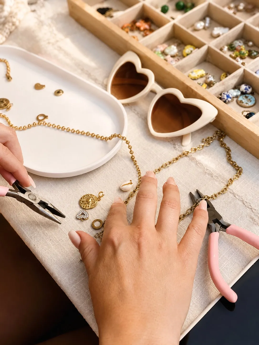 Mains tenant une pince au-dessus d’un plateau de charms, à côté de lunettes en forme de cœur