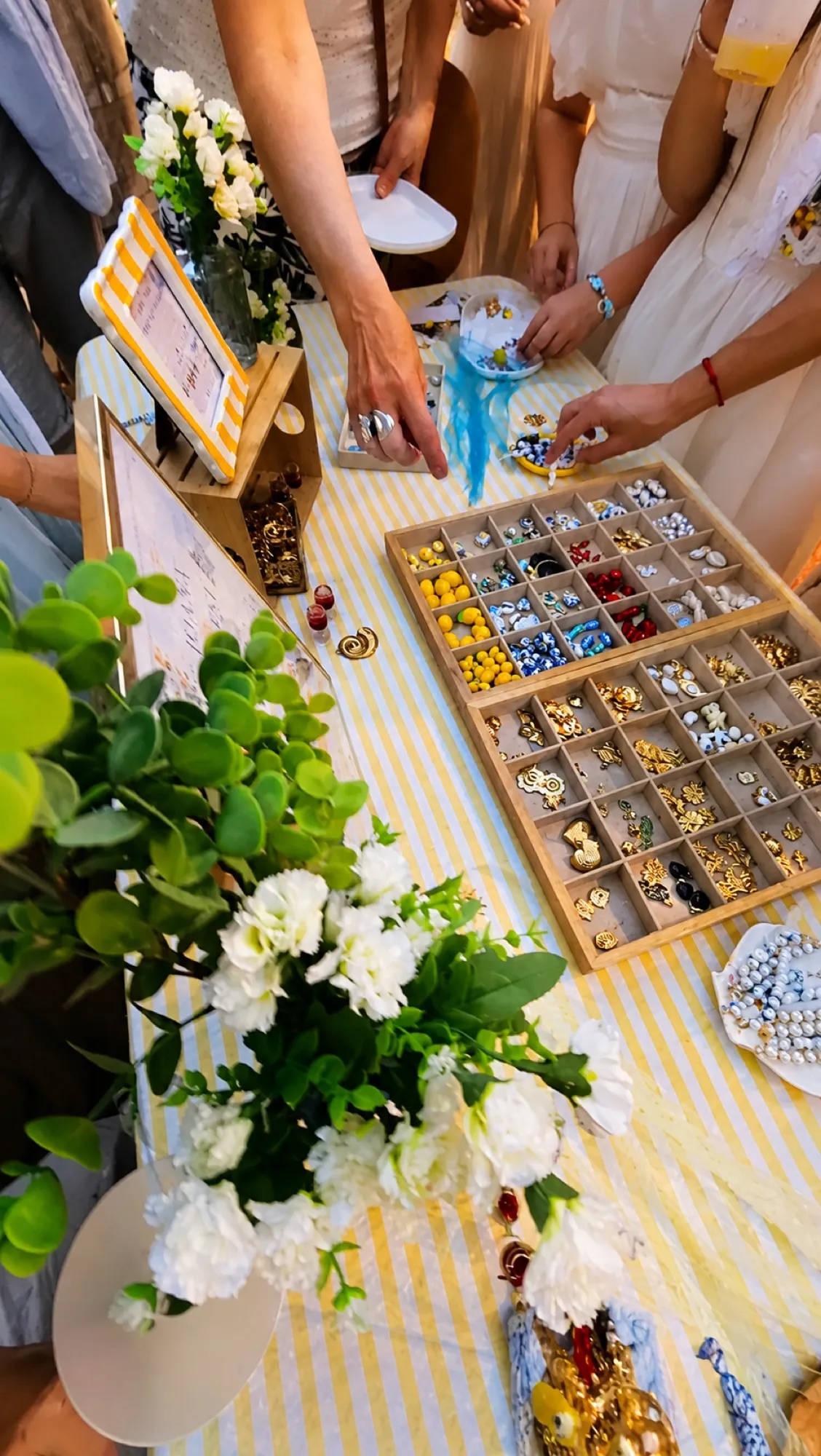 Invitées choisissant leurs charms autour du plateau, parmi les fleurs blanches