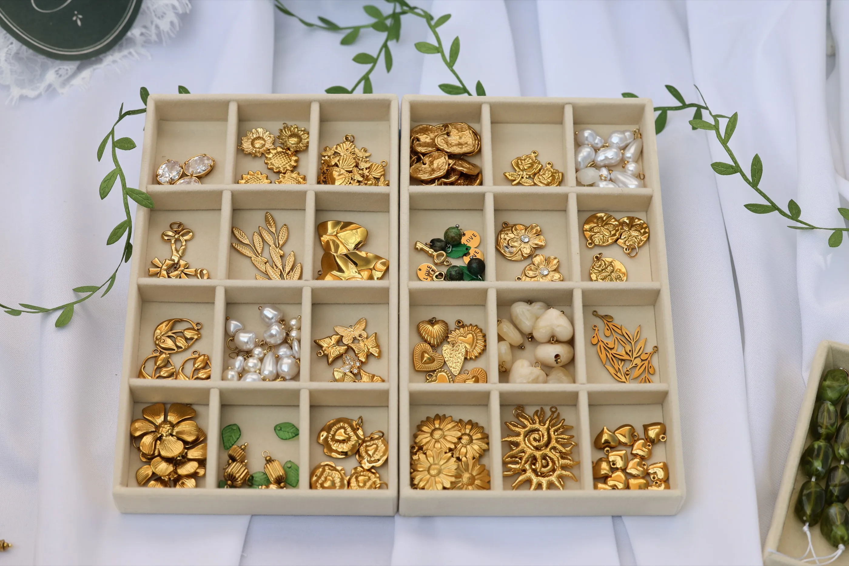 Plateaux de charms dorés, perles et feuillage, posés sur le drapé blanc