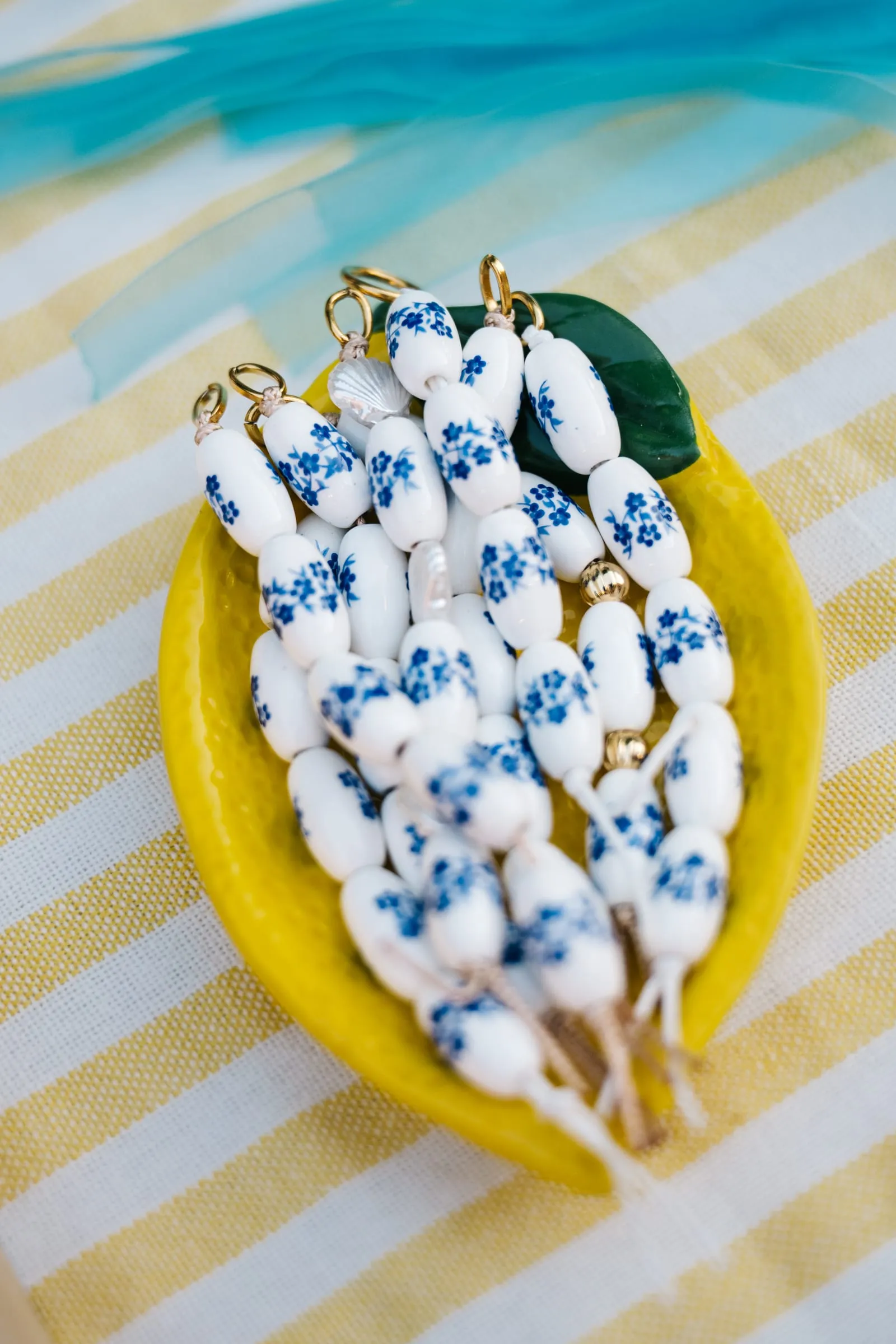 Bijoux terminés, perles blanches et bleues, posés sur une assiette jaune citron