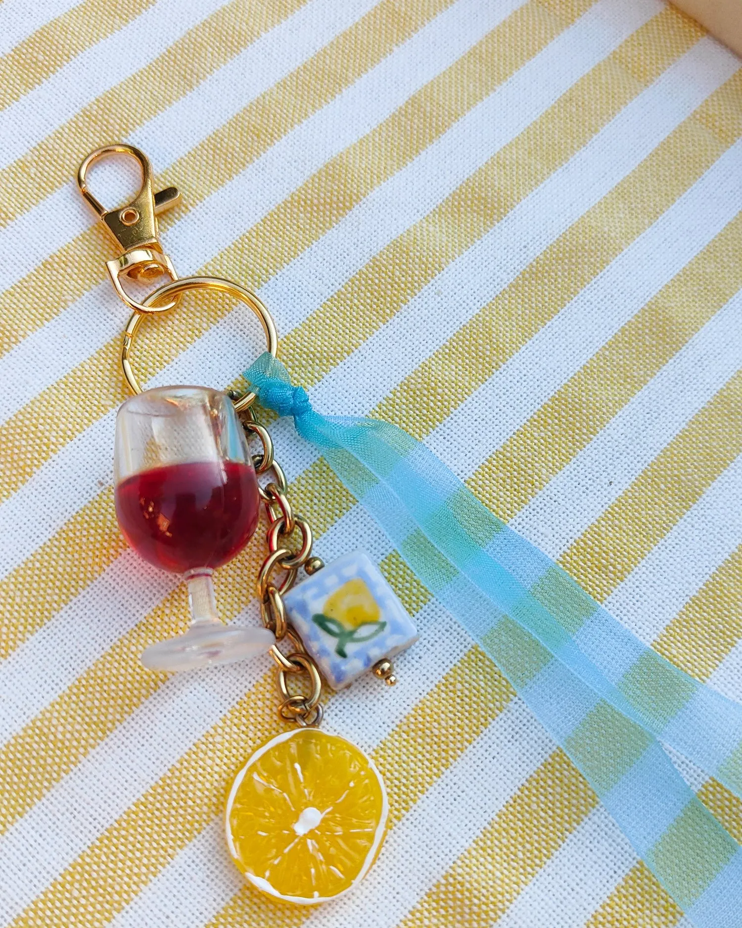 Un porte-clés terminé sur la nappe rayée : verre de vin, rondelle de citron et ruban azur
