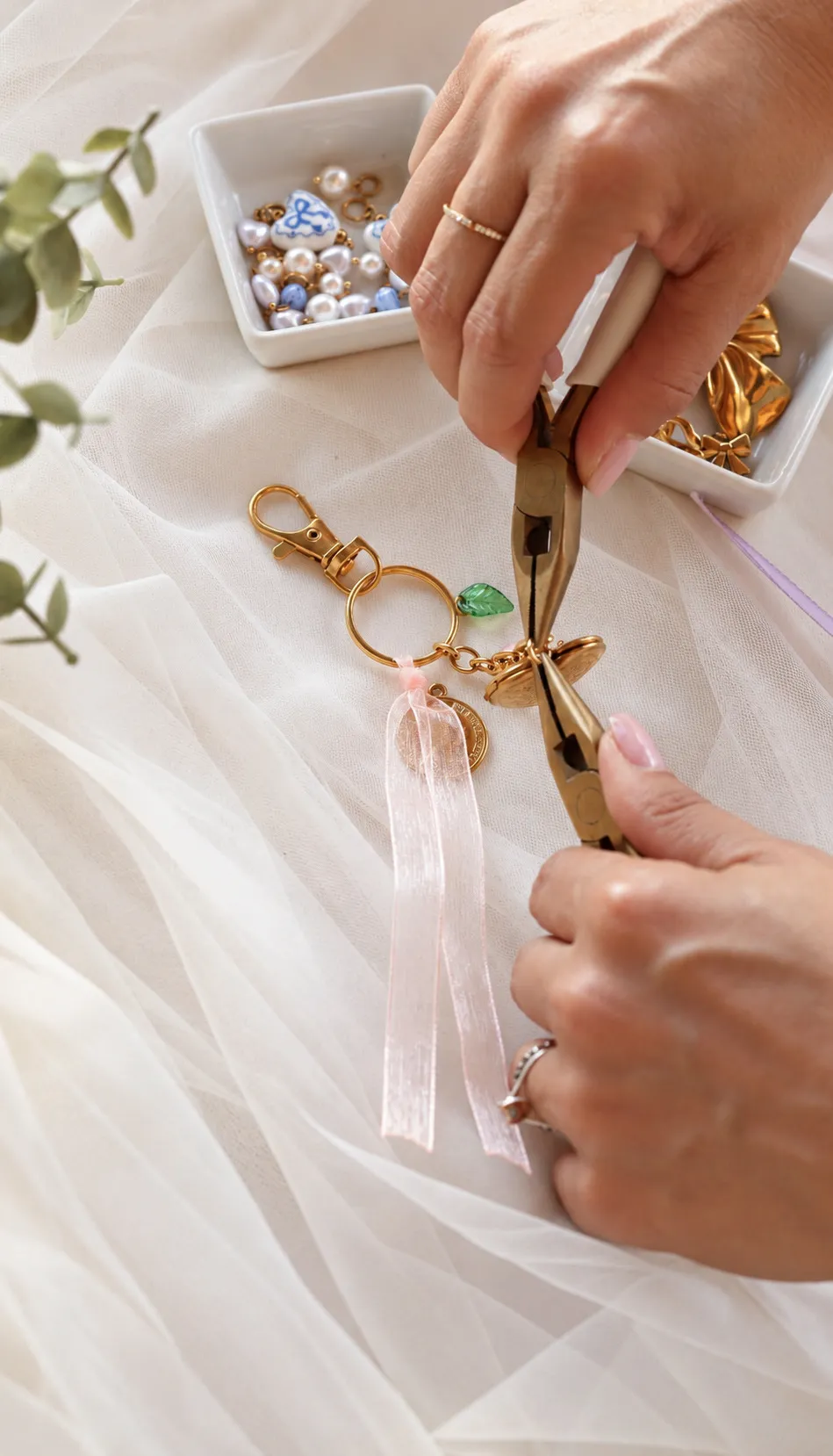 Mes mains assemblant un porte-clés à la pince, au-dessus du plateau de charms