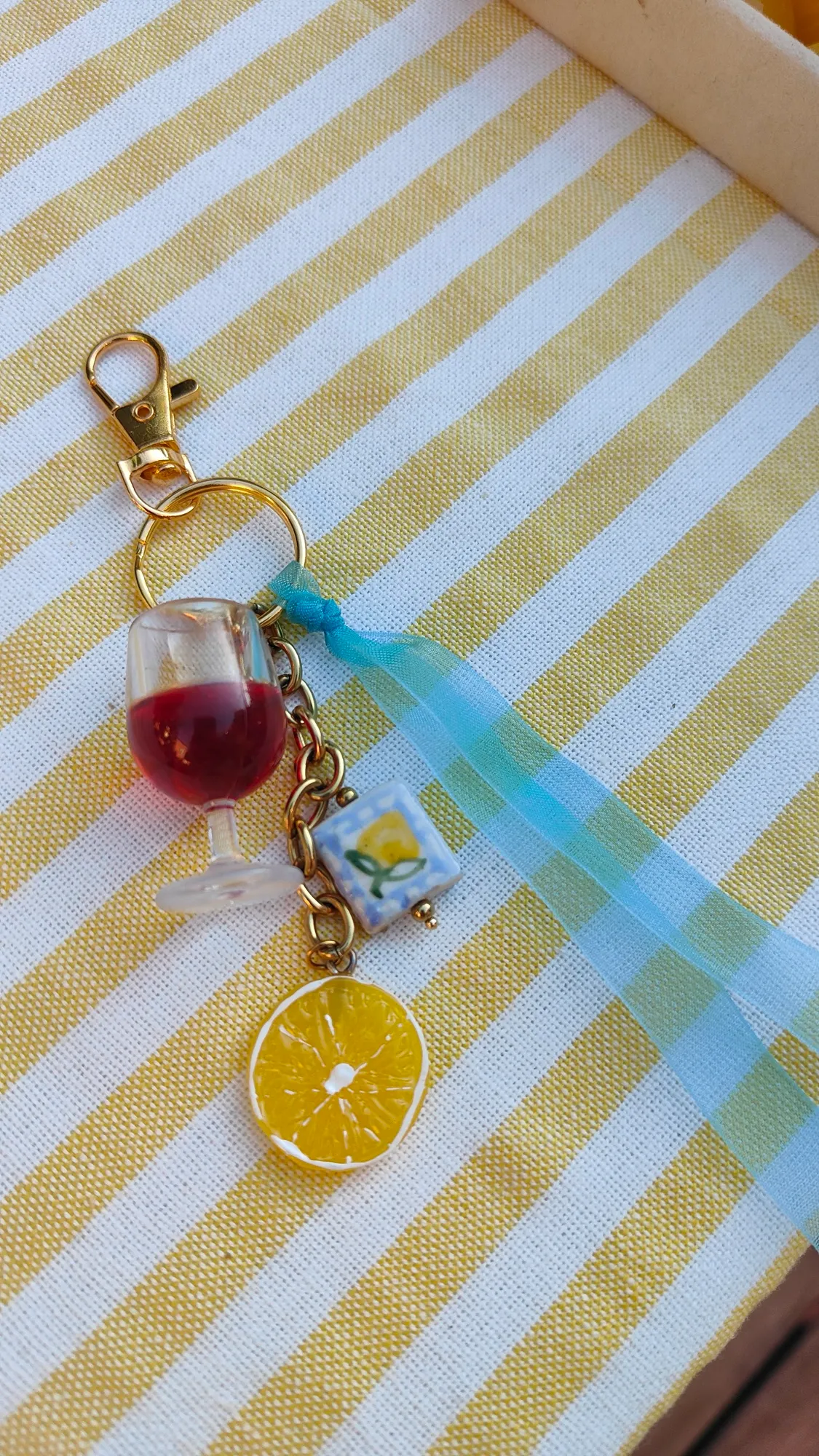 Porte-clés terminé avec verre à vin, rondelle de citron et ruban azur, sur une nappe rayée