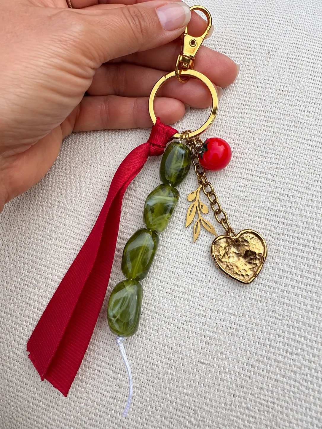 Un porte-clés terminé tenu en main : ruban rouge, perles vertes et cœur doré