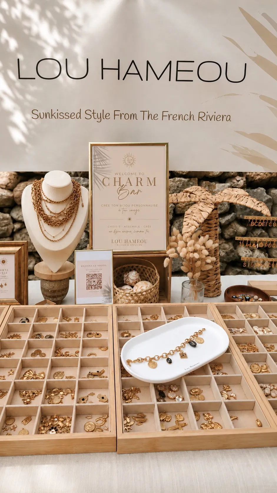 Stand Charm Bar Lou Hameou avec banderole et affiche « Welcome to Charm Bar », plateaux de charms dorés et présentoir à bijoux